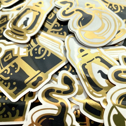 Gold foil stickers of various dark academia designs, including a book, a lantern, and coffee with a snake
